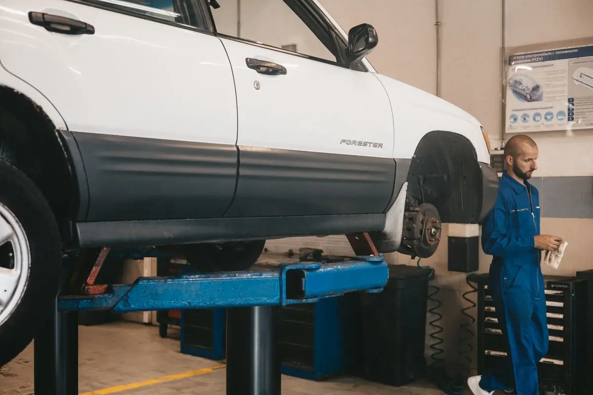 Lift üzerinde ön tekerleği sökülmüş araç ve periyodik bakım yapan servis teknisyeni